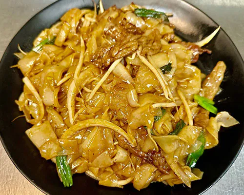 Stir-fried beef chow fun with bean sprouts and scallions on a black plate