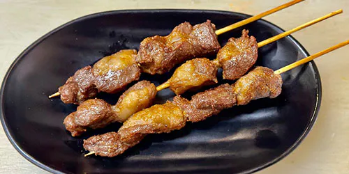Grilled beef skewers with seasoning on a black oval plate