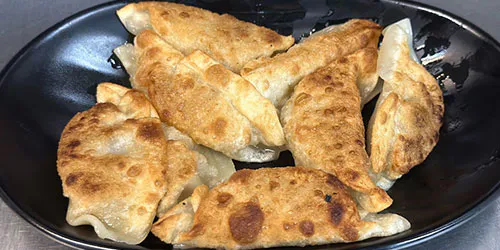 Crispy pan-fried dumplings arranged on a black plate