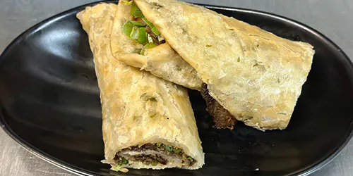 Crispy beef wraps with scallions on a black oval plate