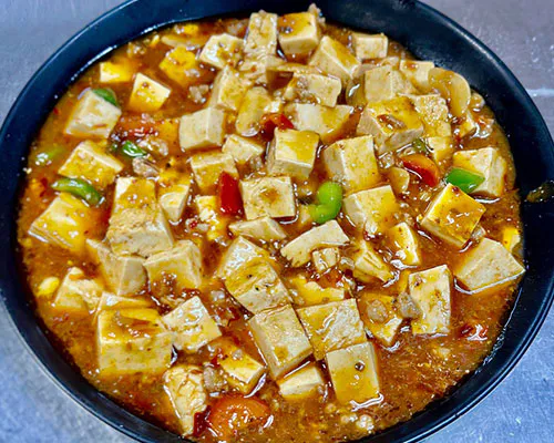 Mapo tofu with spicy sauce, peppers, and minced meat in a black bowl